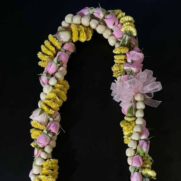 Floral lei with pink buds, yellow flowers, and white beads on a black background
