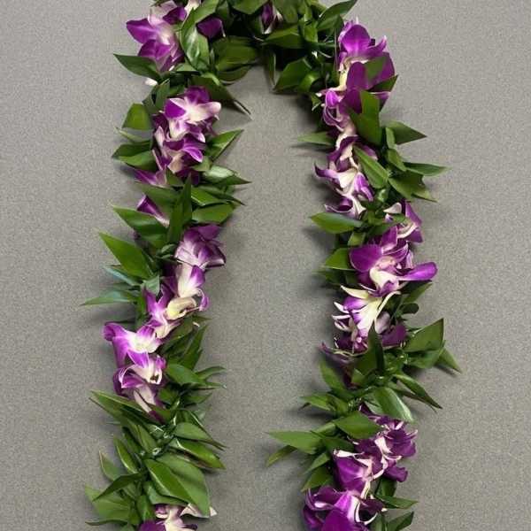 Purple orchid lei with green leaves laid on a gray surface