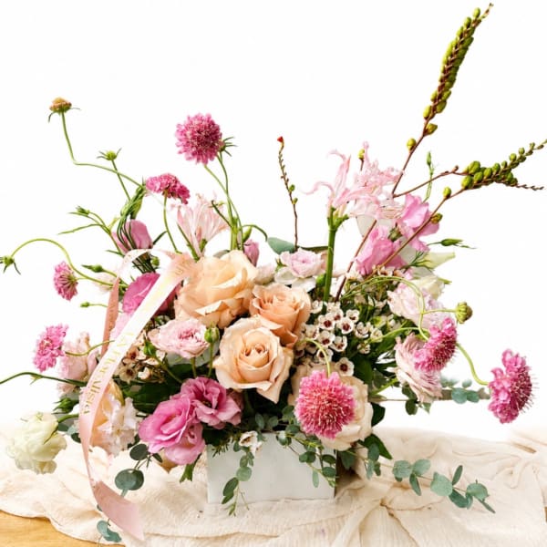 Pink and peach floral arrangement in a white box with a ribbon