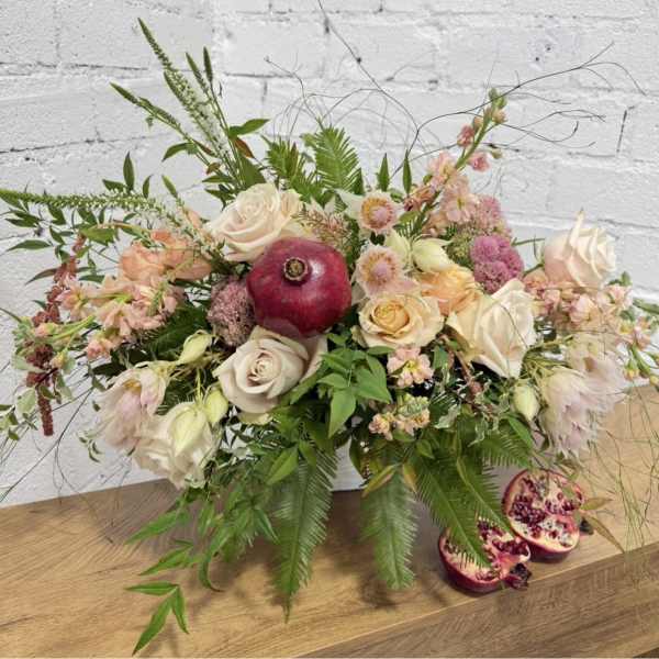 Low floral arrangement with cream and blush roses and a pomegranate centerpiece