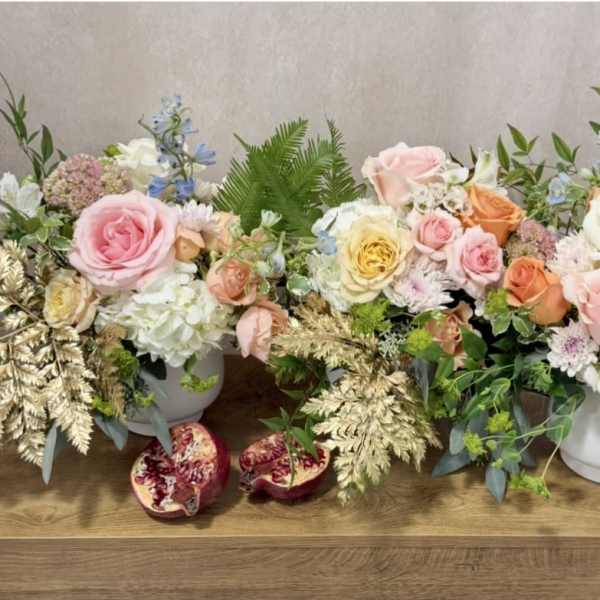 Two pastel floral arrangements in white vases with pomegranates on a table
