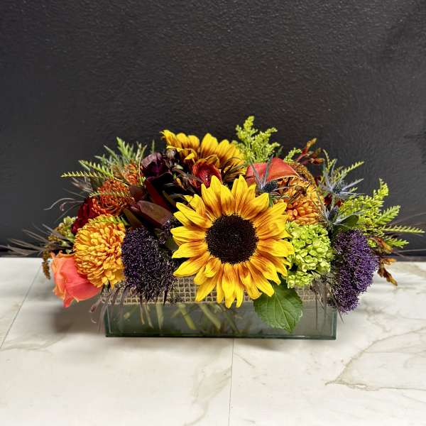 Mixed bouquet with sunflowers, roses, and chrysanthemums in a rectangular glass vase