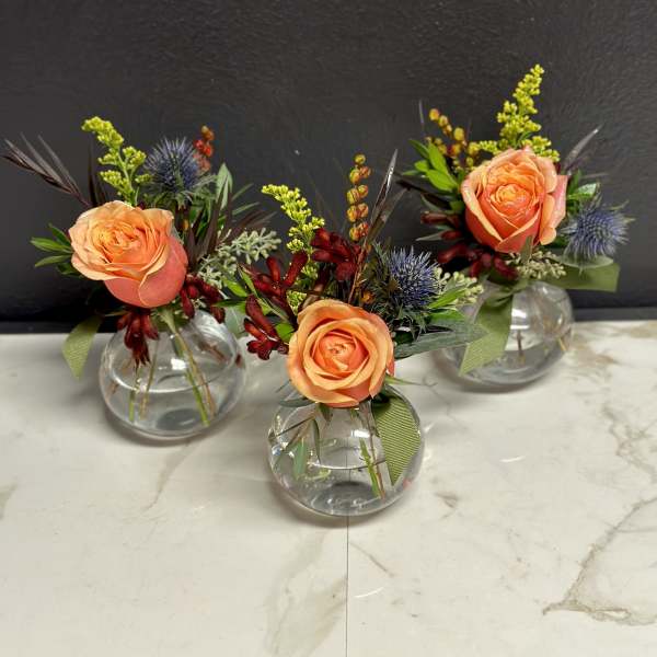 Three small floral arrangements in round glass vases with peach roses