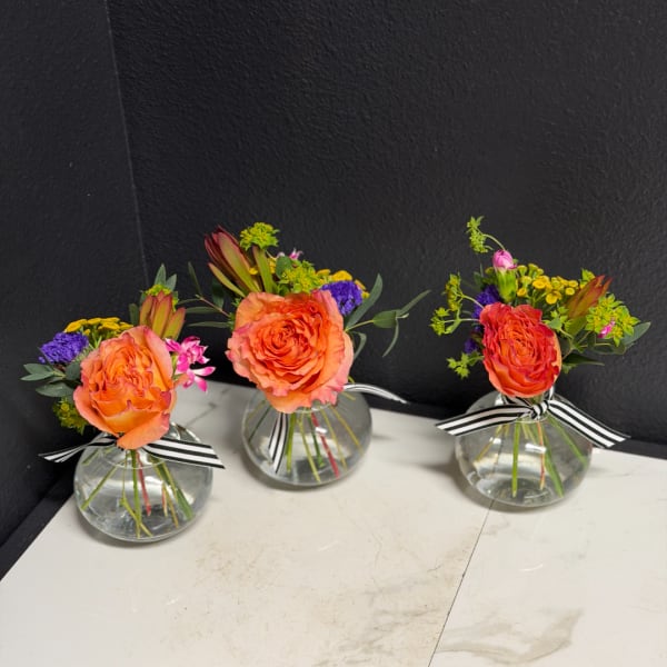 Three small rose arrangements in round glass vases with striped ribbons