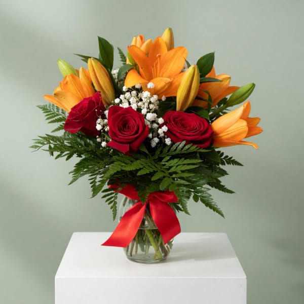 Bouquet of orange lilies and red roses in a glass vase with a red ribbon