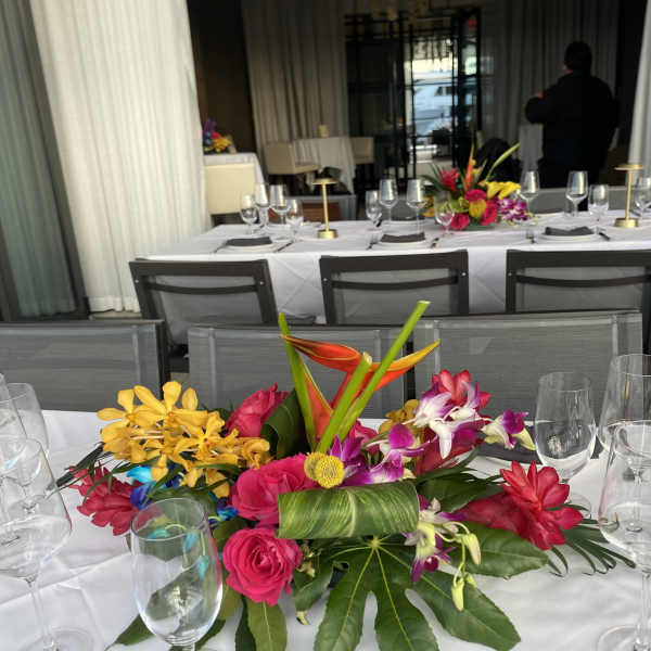 Bright tropical centerpiece with orchids, roses, and bird-of-paradise on a banquet table