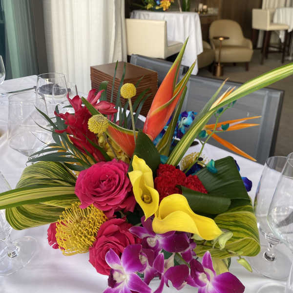 Bright tropical centerpiece with orchids, calla lilies, and roses on a dining table