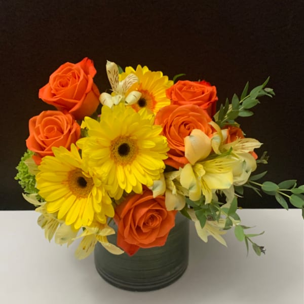 Orange roses and yellow gerbera daisies in a dark vase