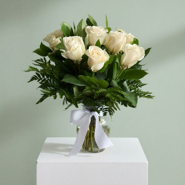 White roses in a glass vase with a white ribbon