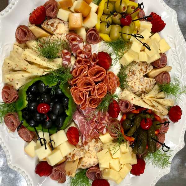 Charcuterie platter with cheeses, olives, strawberries, and rolled meats on a white tray
