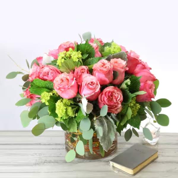Pink rose bouquet in a glass vase with greenery on a white table