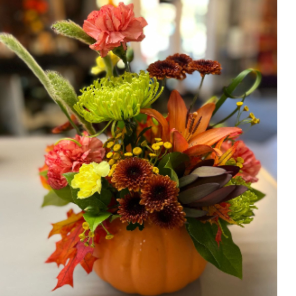 Fall floral arrangement in a pumpkin container with orange, yellow, and pink blooms