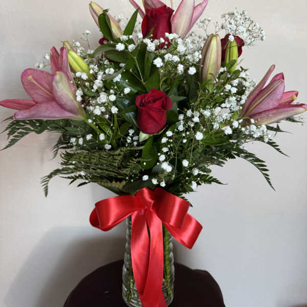 Pink lilies and red roses in a glass vase with a red ribbon