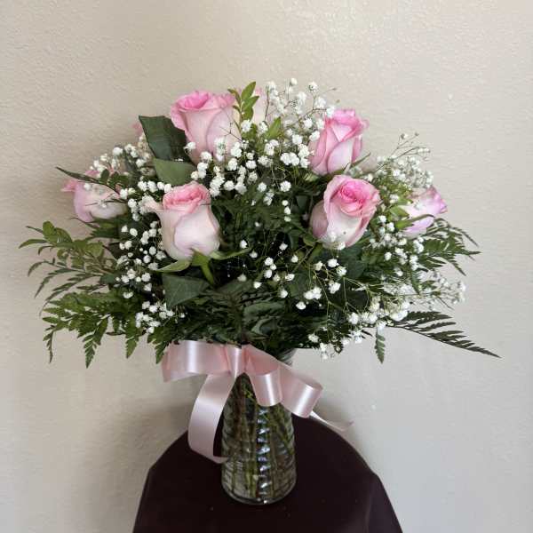 Pink roses and baby's breath in a glass vase with a pink ribbon