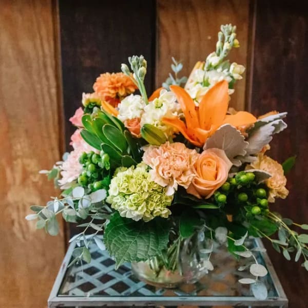 Mixed bouquet with orange lilies, peach roses, and green hydrangeas in a glass vase