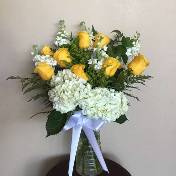 Yellow roses and white hydrangeas in a glass vase with a white ribbon