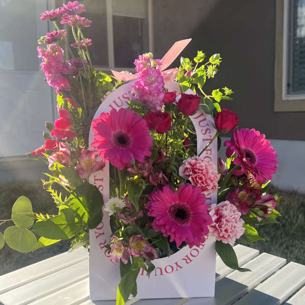 Pink gerbera daisies and roses arranged in a white gift bag