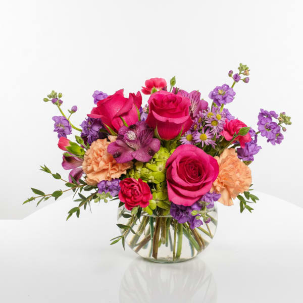 Mixed bouquet of pink and purple flowers in a round glass vase