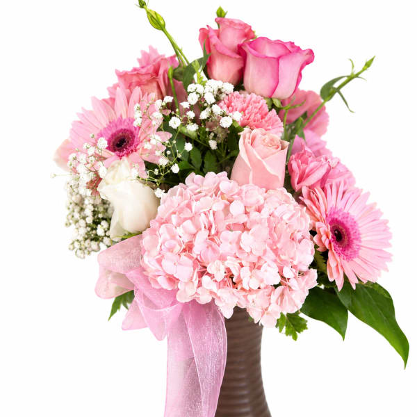 Pink roses and gerbera daisies in a brown vase with a pink ribbon