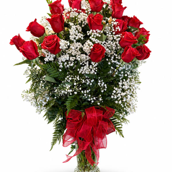Red roses and baby's breath in a clear glass vase with a red ribbon