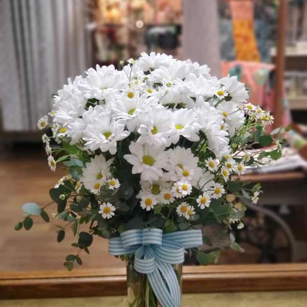 White daisy bouquet in a clear glass vase with a blue striped ribbon