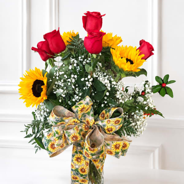 Red roses and yellow sunflowers in a glass vase with a sunflower ribbon