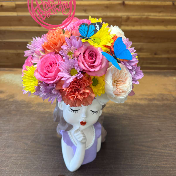 Colorful flower arrangement in a decorative girl-shaped vase with butterfly picks
