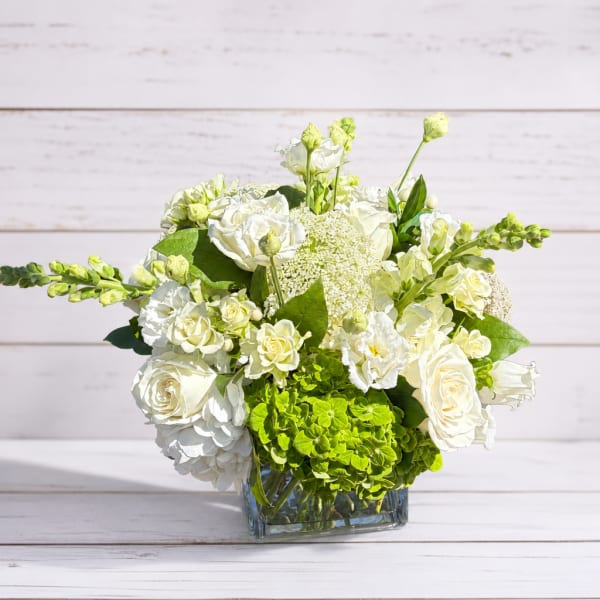 White roses and green hydrangeas in a clear square vase