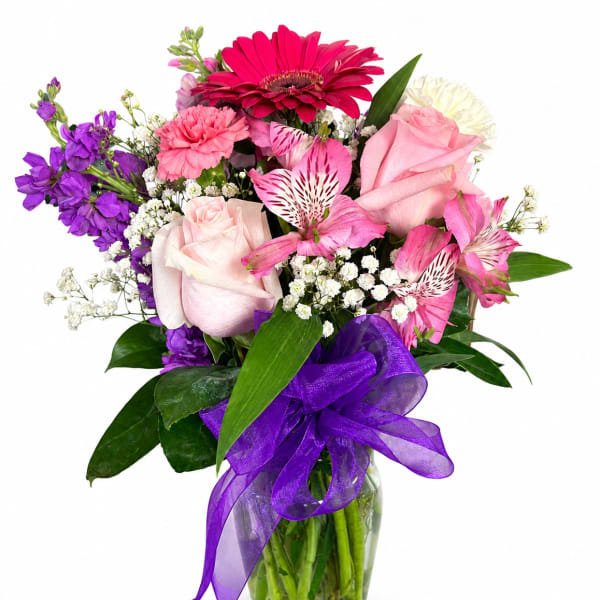 Mixed bouquet of pink, purple, and white flowers in a glass vase with a purple ribbon