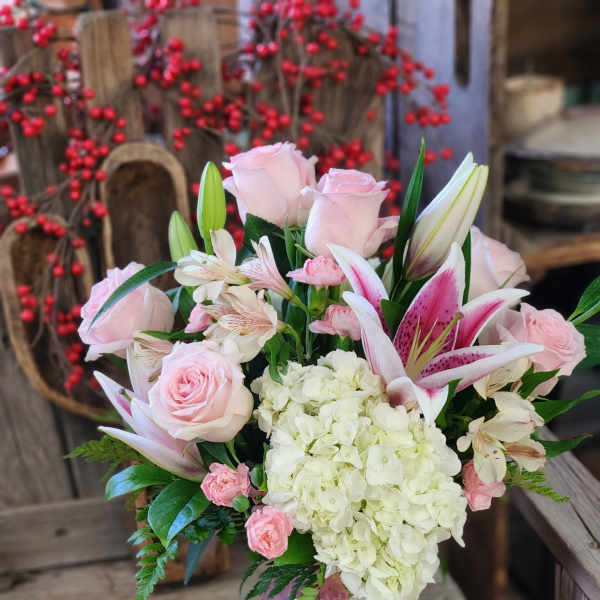 Pink and white bouquet with roses, lilies, carnations, and hydrangeas in a pink vase.
