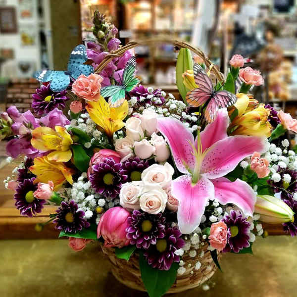 Basket arrangement of pink lilies, roses, and purple daisies with butterfly picks