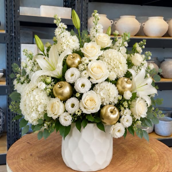 White floral arrangement with roses, lilies, and gold apple accents in a white vase