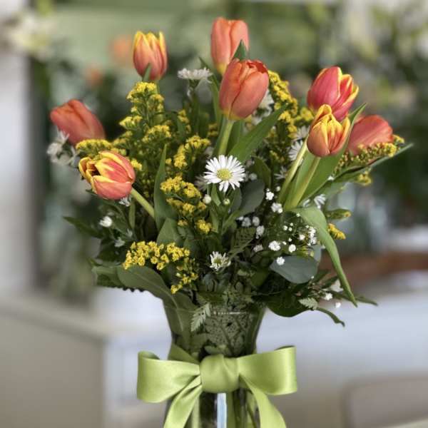 Bouquet of coral tulips and small white daisies in a glass vase with a green ribbon