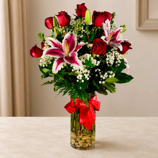 Red roses and pink lilies in a glass vase with a red ribbon
