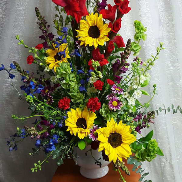 Tall mixed bouquet with sunflowers, red gladiolus, and blue flowers in a white vase