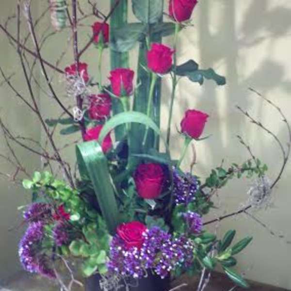 Tall arrangement of pink roses and purple flowers in a black container