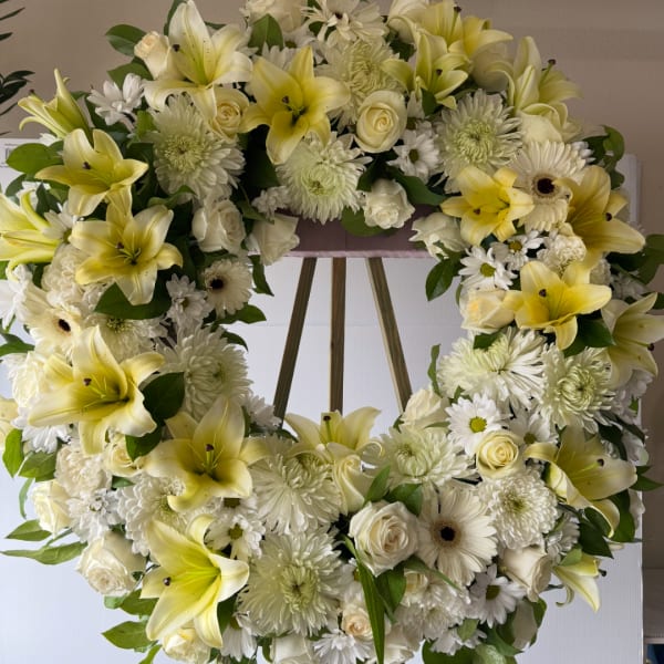 Heart-shaped floral wreath with yellow lilies, white roses, and white daisies