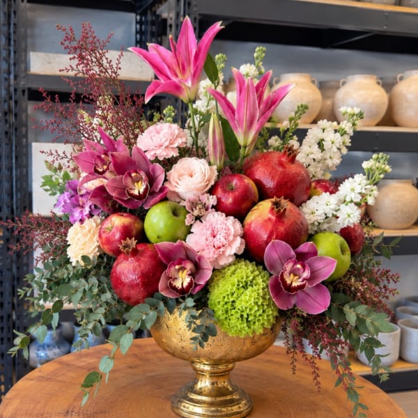 Mixed floral arrangement with orchids, apples, and pomegranates in a gold vase