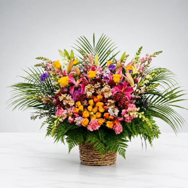 Large mixed flower arrangement in a woven basket with palm fronds