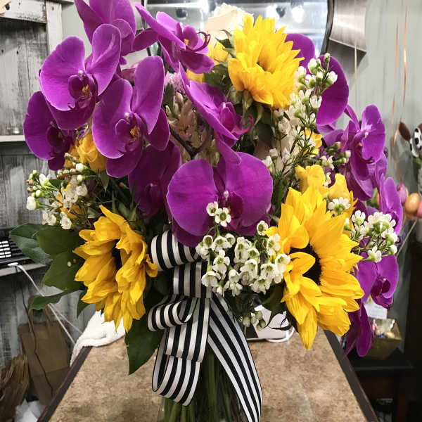 Bouquet of purple orchids and yellow sunflowers in a glass vase with a striped ribbon