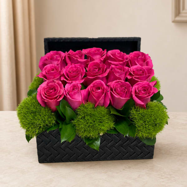 Pink roses arranged in a black woven box with green moss accents
