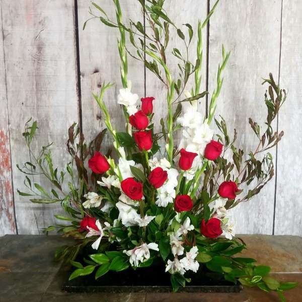 Tall floral arrangement with red roses and white flowers in a low black container