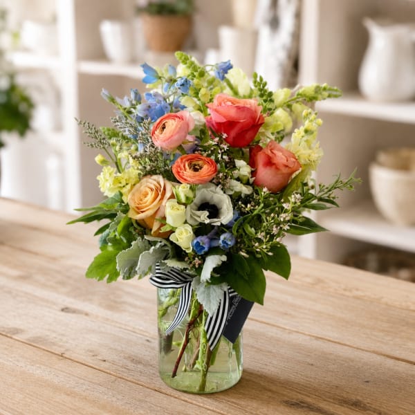 Mixed bouquet of roses, ranunculus, and blue flowers in a glass vase