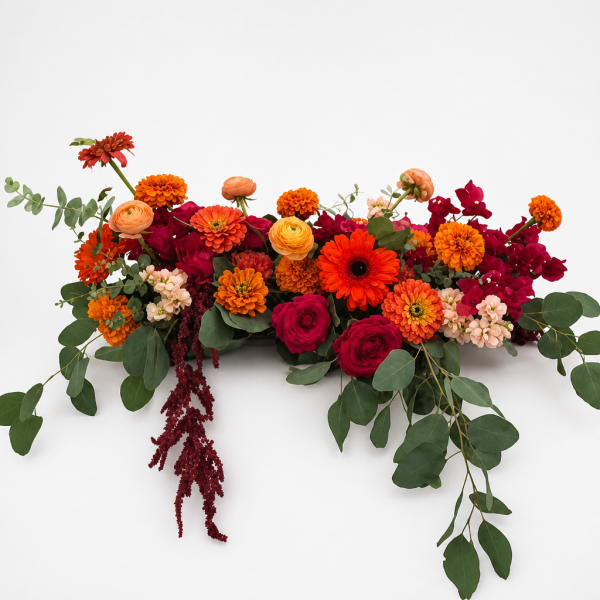 Long low arrangement of orange, red, and pink flowers with trailing greenery