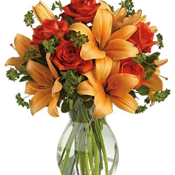 Orange lilies and red roses arranged in a clear glass vase