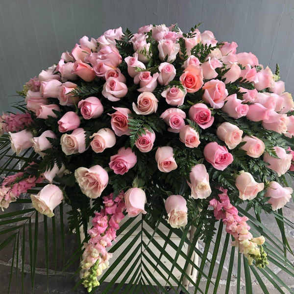 Large pink rose funeral spray with cascading flowers and palm fronds