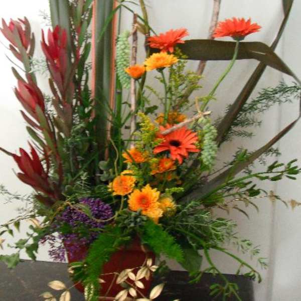 Tall floral arrangement with orange gerbera daisies and red tropical blooms