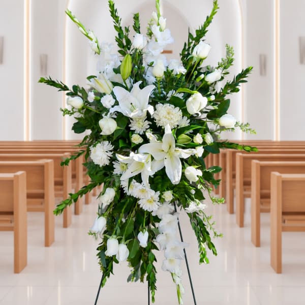 White floral standing spray on an easel in a church aisle
