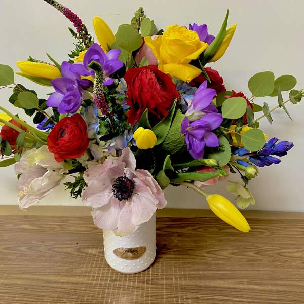 Colorful mixed bouquet in a white vase with red, yellow, purple, and pale pink blooms