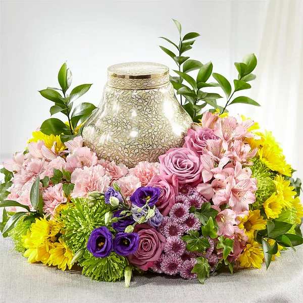 Mixed pink, purple, and yellow floral arrangement around a decorative urn